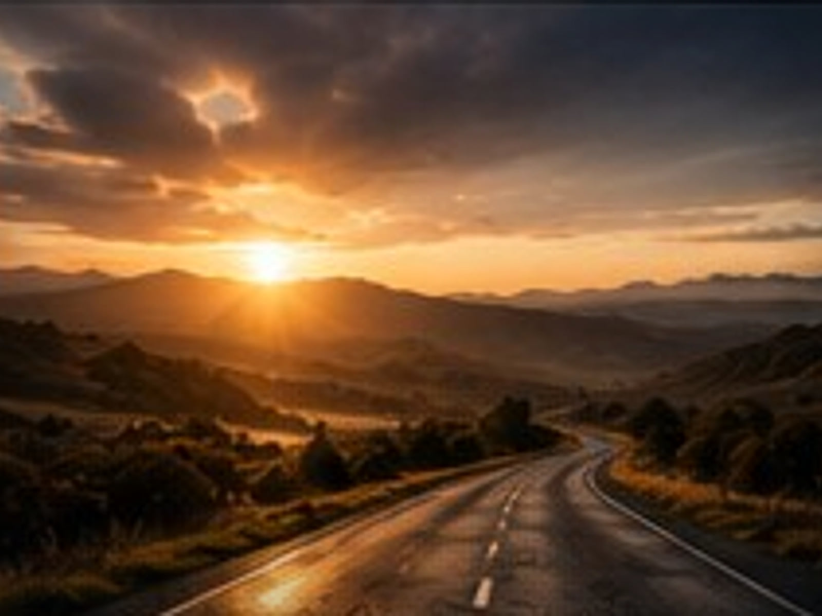An open road winding toward sunrise over distant hills